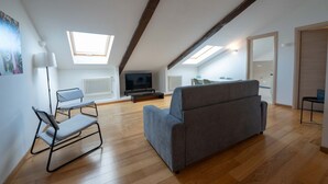 Um apartamento moderno do tipo loft, com teto alto, janelas no teto, um sofá cinzento, uma mesa pequena e uma televisão.