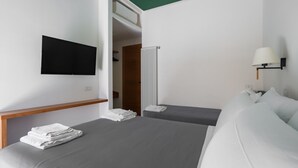 A hotel room with two beds, a TV mounted on the wall, a radiator, and a lamp on the wall. - Weaver Suites 1 By Dimorra (Napoli)