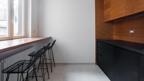 A kitchen with a window, a radiator, black bar stools, and wooden cabinets. - Weaver Suites 1 By Dimorra (Napoli)