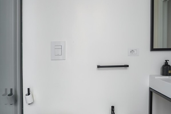 A modern bathroom with a white wall, a towel dispenser, a soap dispenser, a towel rack, and a mirror.