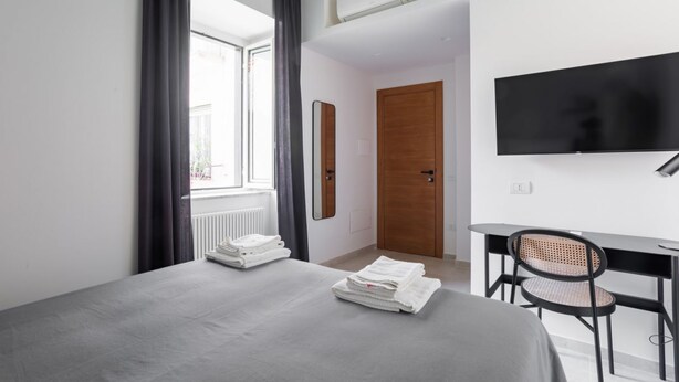 A modern hotel room with a bed, a desk, a chair, a TV, and a door. - Weaver Suites 4 By Dimorra (Napoli)