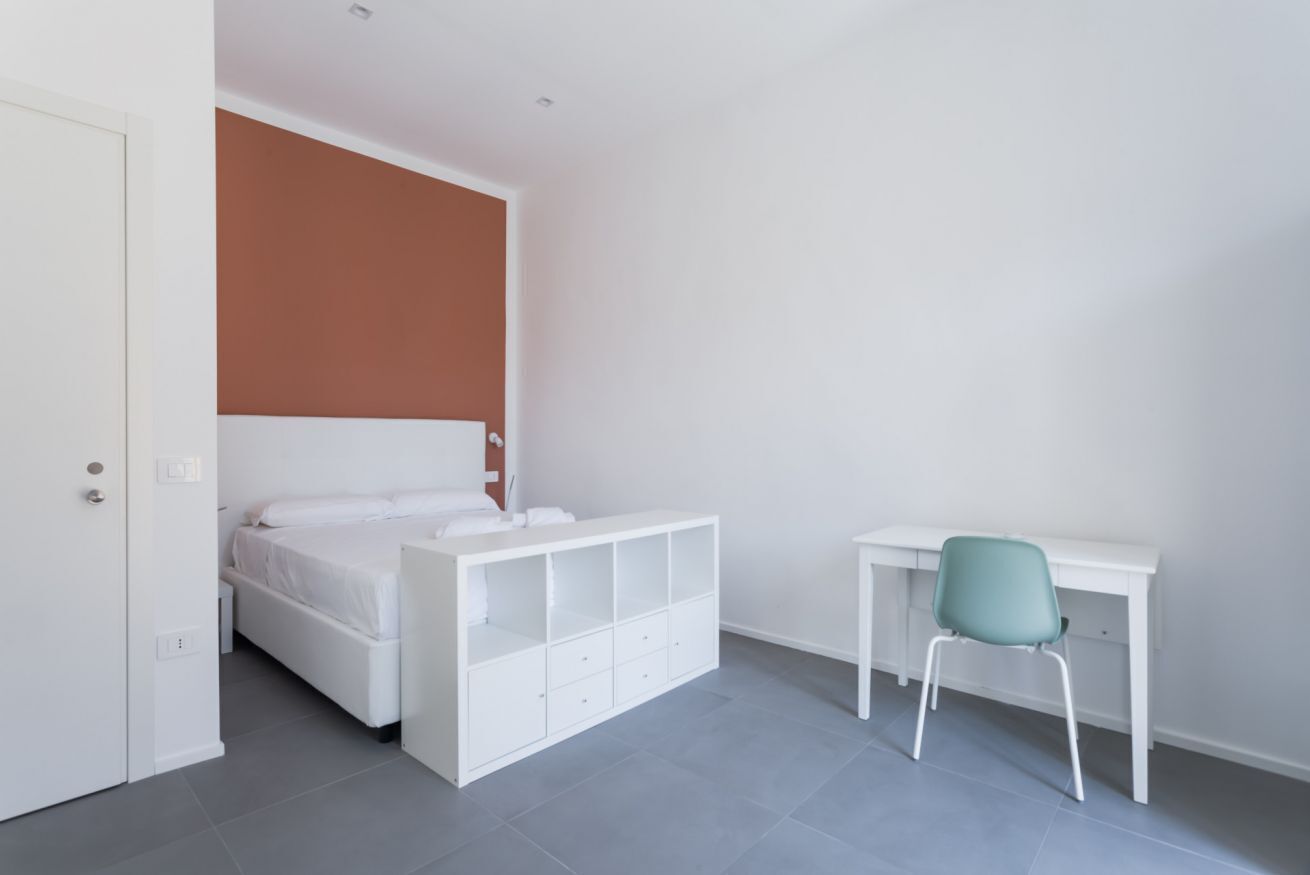 A bedroom with a bed, a desk, and a chair.