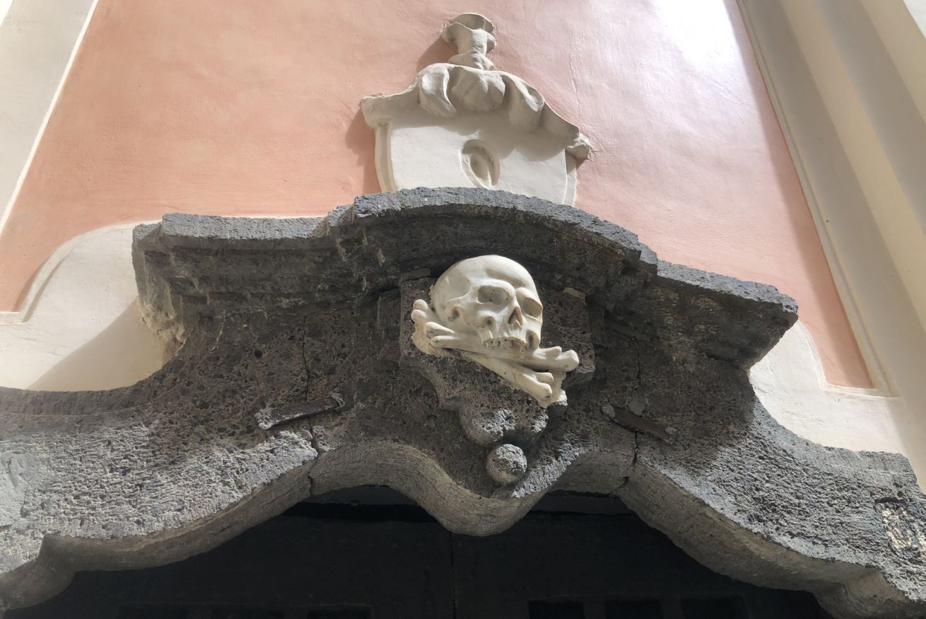 A stone facade with a carved skull and a small figure above it.