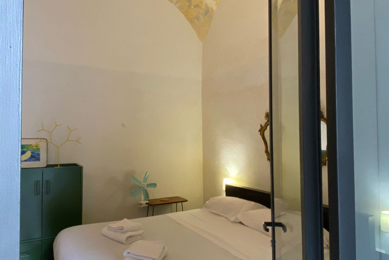 Une chambre d’hôtel avec un lit, une table de chevet, une armoire verte et une plante décorative.