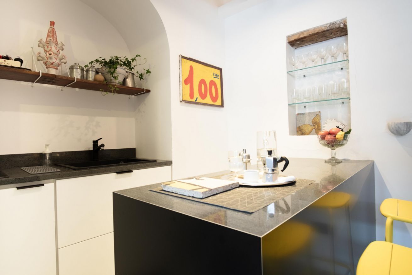 A modern kitchen with a central island, a black countertop, and a yellow chair. A price sign of 100 euros is visible on the wall.
