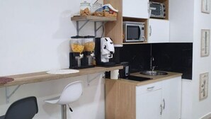 A compact kitchen with a microwave, toaster, and a coffee maker on the countertop. There are shelves above the counter holding jars and a toaster.