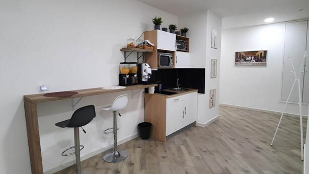 A compact kitchen with a wooden countertop, two white bar stools, a microwave, and a sink.