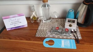 A wooden table with a thank you card, a bottle, glasses, a coffee maker, and a spoon set.