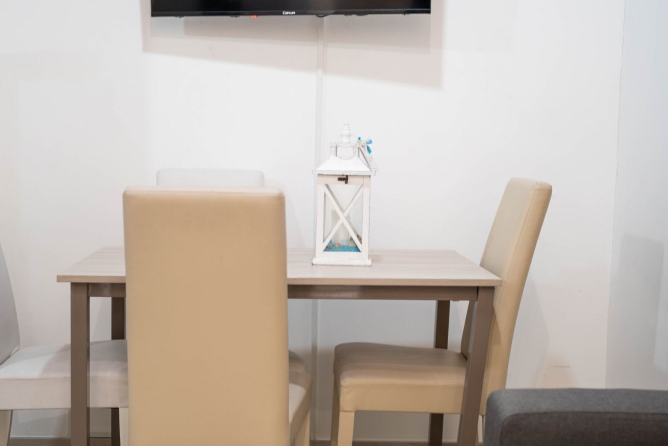 Een eetgedeelte met een tafel, stoelen, een witte lantaarn en een zwart tv-toestel aan de muur.