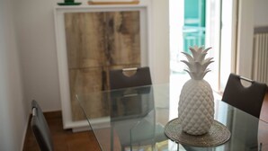 Spiseområde med et glasbord, en hvid ananas som midtpunkt, og udsigt til en bygning gennem et vindue.