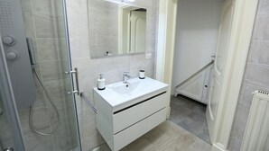 Et moderne badeværelse med en brusekabine i glas, et hvidt toiletbord med spejl og et flisegulv.