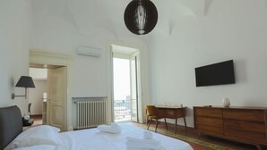 Et hotelværelse med seng, skrivebord, stol, kommode, fjernsyn og radiator.