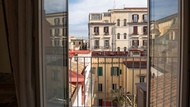 A view from a window with a metal railing, overlooking a row of buildings with balconies and red-tiled roofs. - La Casa di Giulia By Dimorra (Napoli)