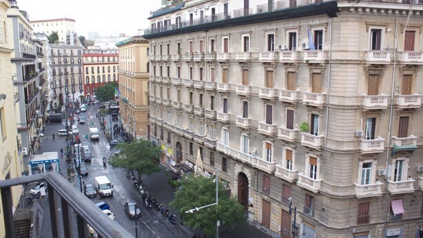 A multi-story building with balconies, a street view, and parked cars.