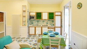 A compact kitchen with a dining area, featuring a patterned floor, a green and white checkered tablecloth, and a white radiator.