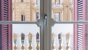 Vista a través de una ventana de metal que muestra la fachada de un edificio de arquitectura clásica, con columnas y molduras decorativas.