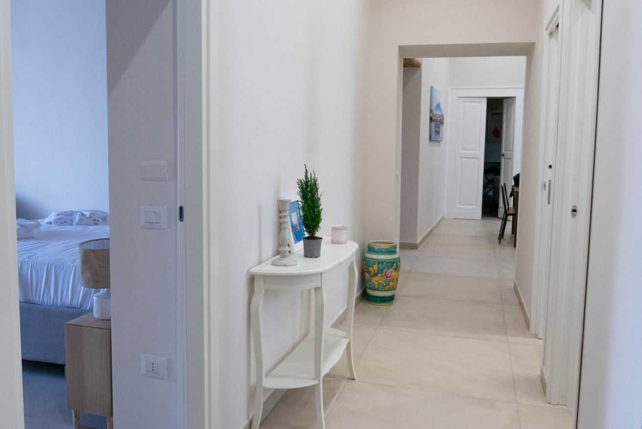Een hal met een bed, een witte console en een plant, en een kleurrijke vaas.