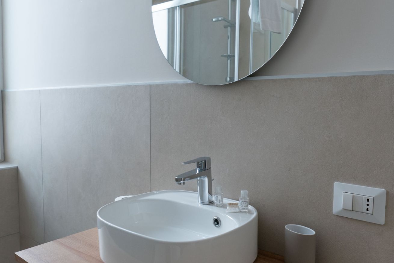 A modern bathroom with a round sink, a mirror, and a light switch on the wall.