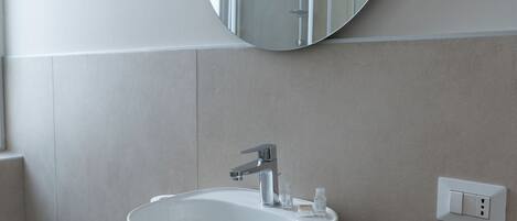A modern bathroom with a round sink, a mirror, and a light switch on the wall.