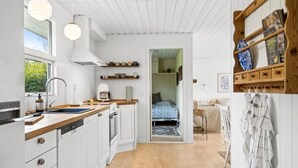 A modern kitchen with white cabinetry, a built-in oven, and a coffee machine. There is a wooden countertop, a sink, and a window providing natural light.