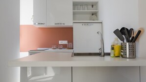 A modern kitchen with white cabinets, a white countertop, and a sink. There are kitchen utensils in a holder and a clock on the wall. - Mare Fiore Room By Dimorra (Napoli)