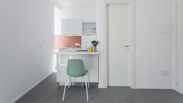 A modern kitchen with white cabinets, a green chair, and a door to another room. - Mare Fiore Room By Dimorra (Napoli)
