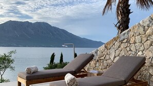 A poolside area with two lounge chairs, a stone wall, and a view of a lake and mountains.
