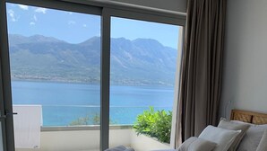 A bedroom with a bed, a view of a lake and mountains, and a balcony with a plant.