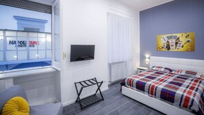 Een moderne hotelkamer met een bed, een televisie, een raam met uitzicht op een gebouw en een schilderij aan de muur.
