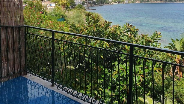 A balcony with a view of a coastal town, a mountain, and a clear sky.