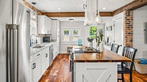 Una cocina moderna con armarios blancos, una mesa de comedor de madera y una pared decorativa de ladrillo.