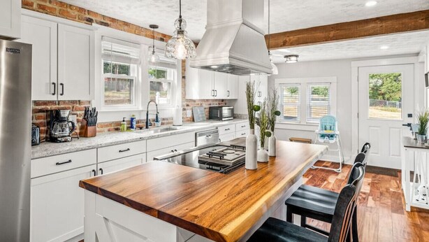 Una cocina moderna con gabinetes blancos, una isla de madera y una pared decorativa de ladrillo.
