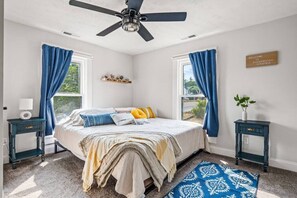 A bedroom with a bed, two nightstands, a ceiling fan, a window with curtains, a welcome sign, and a small plant. - Modern Farmhouse w/ Hot Tub, Close to SNP (Shenandoah)