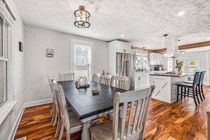 A dining area with a wooden table and chairs, a chandelier, and a kitchen in the background. - Modern Farmhouse w/ Hot Tub, Close to SNP (Shenandoah)