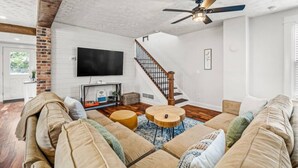 Un salón amplio con un sofá grande, dos mesitas redondas, una chimenea y un televisor montado en la pared.