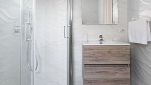Un baño moderno con cabina de ducha de vidrio, tocador de madera y un espejo grande.
