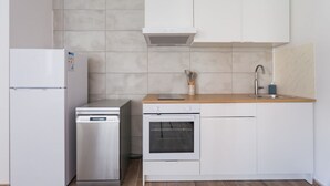 Cocina compacta con armarios blancos, lavavajillas de acero inoxidable, horno empotrado y encimera de madera.