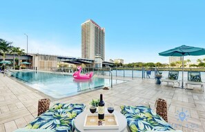 A rooftop pool area with lounge chairs, a pink flamingo float, and a bottle of wine on a tray.