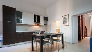 Une cuisine moderne avec des meubles de rangement aux couleurs sombres, une table à manger avec des chaises et un robinet apparent.