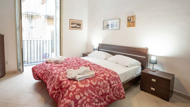 Une chambre à coucher avec un lit, une table de chevet et une fenêtre donnant sur des immeubles.