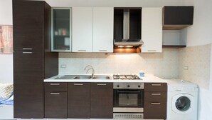 Une cuisine moderne avec des meubles de couleur brun foncé, une hotte de cuisinière en acier inoxydable, un four encastré, un évier et un lave-linge à chargement frontal.