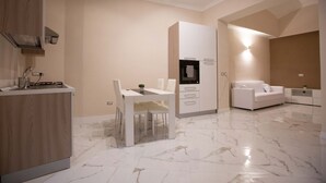 Une cuisine moderne dotée d’un plan de travail en marbre, d’un four encastré et d’un coin repas avec une table et des chaises blanches.