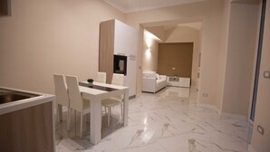 Une cuisine moderne avec des meubles blancs, un coin repas doté d’une table et de chaises blanches, et un sol en marbre.