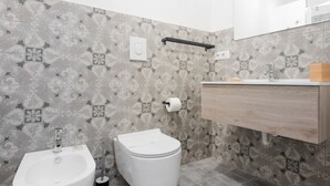Un baño con bidé, inodoro y lavamanos con tocador de madera.