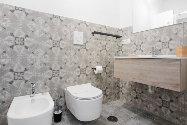 A bathroom with a bidet, toilet, and sink with a wooden vanity.