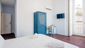 Habitación de hotel con cama, armario azul, escritorio con silla y televisor en la pared.