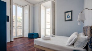 Un dormitorio con una cama grande, un reposapiés azul y vistas a través de un ventanal.