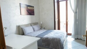A bedroom with a bed, a desk, and a nightstand. There is a window with curtains and a door leading to an outdoor area. - Suite Orchidea by Dimorra (Napoli)