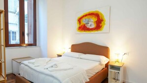 Een hotelkamer met een bed, twee nachtkastjes, een raam met jaloezieën en een schilderij aan de muur.