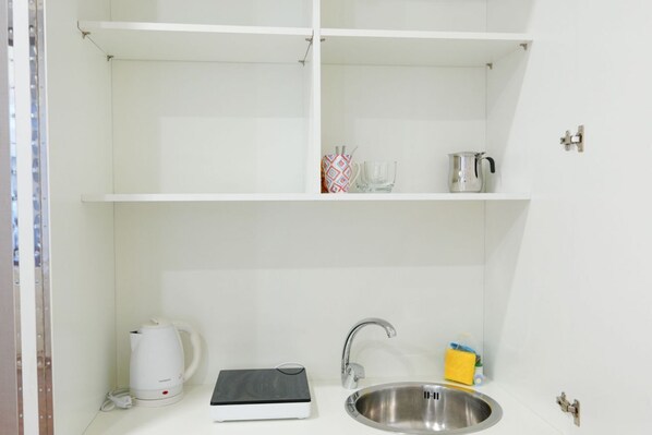 A compact kitchenette with a stainless steel sink, a kettle, a coffee maker, and a small shelf with a few items.